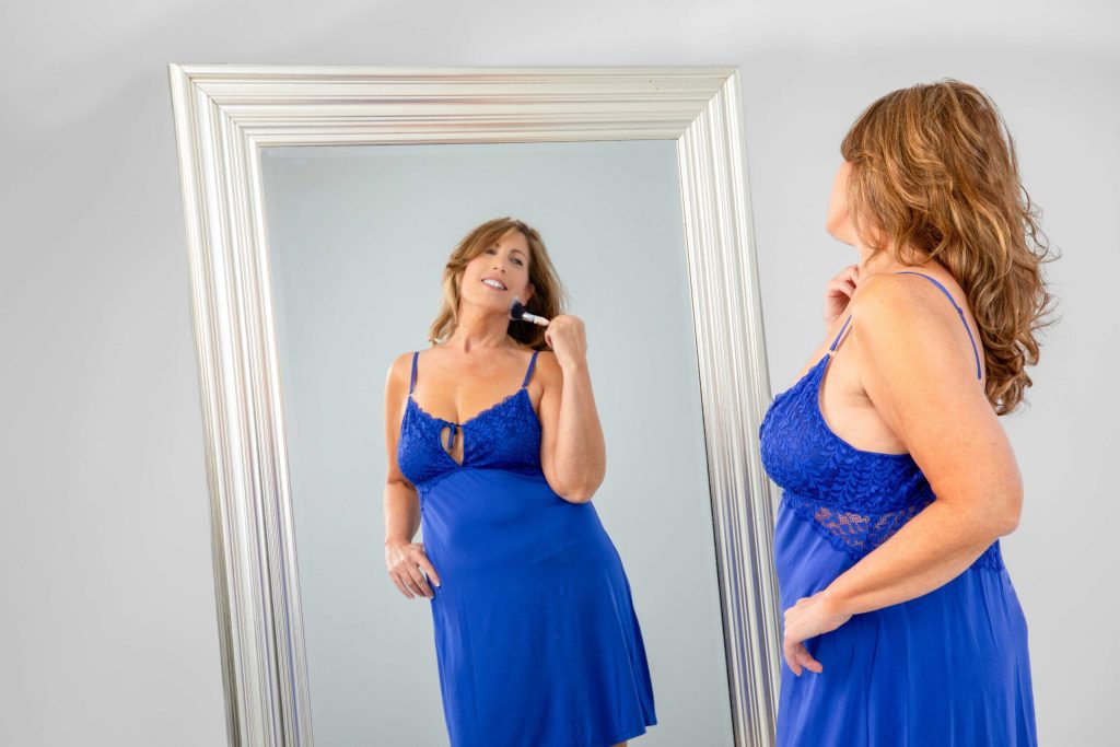 Woman admiring herself in the mirror wearing Deborah Winthrop's elegant blue evening gown